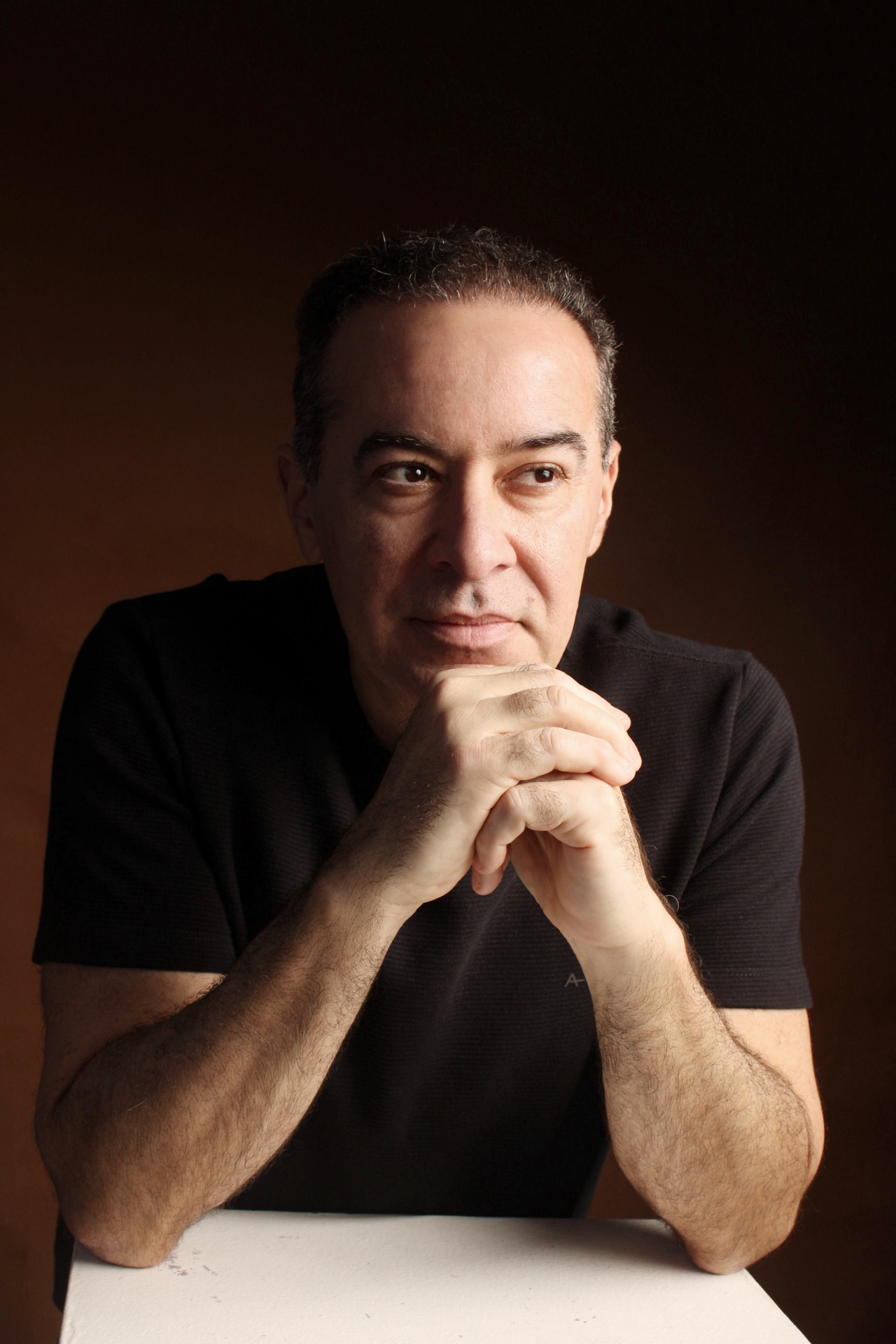 Dr. Glauco Almeida, cirurgião plástico, com as mãos entrelaçadas em retrato sóbrio